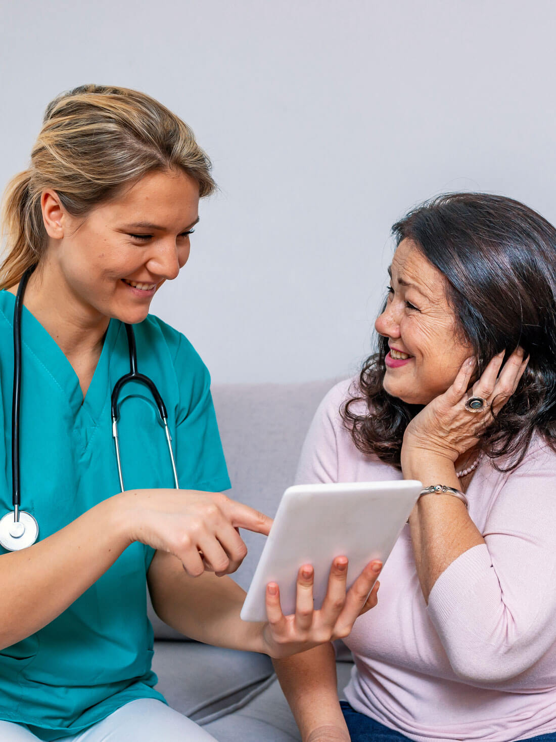 Happy Young Caregiver And Senior Woman Using Digital Tablet Toge